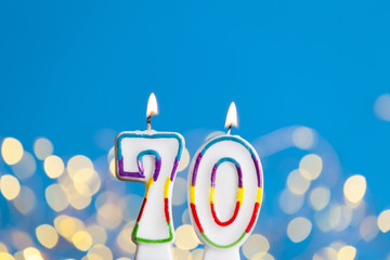 Number 70 birthday celebration candle against a bright lights and blue background