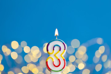 Number 3 birthday celebration candle against a bright lights and blue background