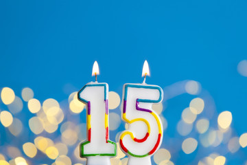 Number 15 birthday celebration candle against a bright lights and blue background