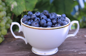 Closeup on a tasty ripe freshly picked blueberries in a white vintage ceramic bowl. Selective focus, free text space. Fruits harvested in summer. Healthy fruit,blurred background.