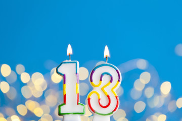 Number 13 birthday celebration candle against a bright lights and blue background