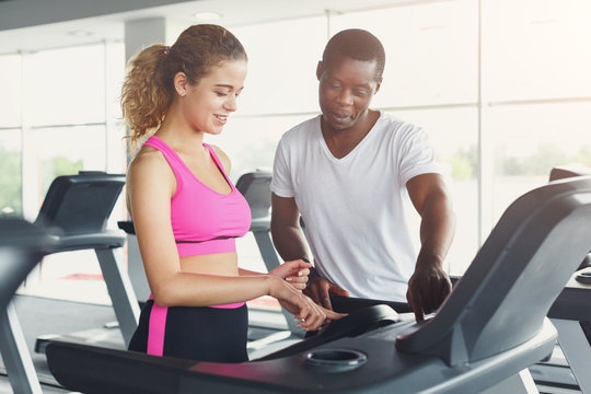 Fitness instructor helps young woman on treadmill
