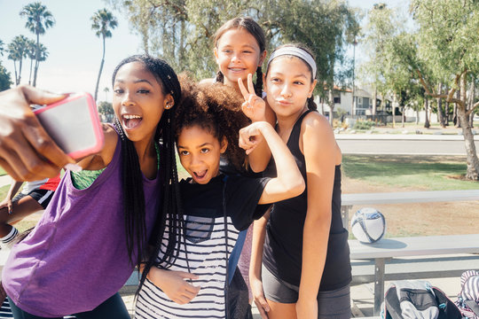 Schoolgirl soccer players taking smartphone selfie on school sports field