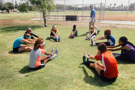 Teacher instructing schoolgirl soccer players in warm up on school sports field