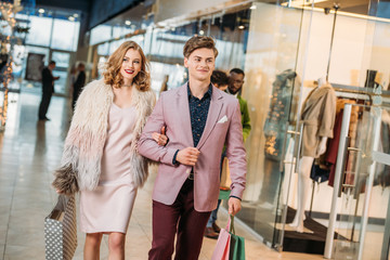 happy stylish young couple with shopping bags walking together in mall