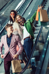 happy young multiethnic shoppers on escalator at mall with packages