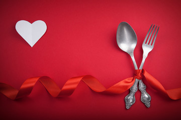 Vintage spoon and fork with a red tape and white heart for Valentine's day on a red background.