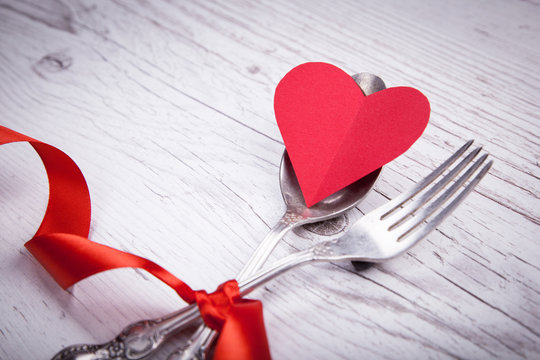 Vintage spoon and fork with a red tape and heart for Valentine's day on a wooden table.