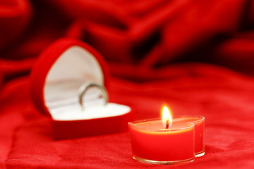 One candle in shape of heart on red silk background