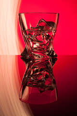 Cocktail whiskey a glass with pieces ice of party reflection a concept of hourglasses yellow light effects on red background.