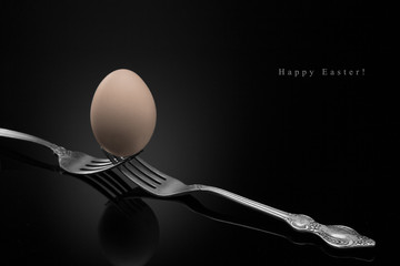 Happy Easter,yellow egg two forks ancient silver on a black background.