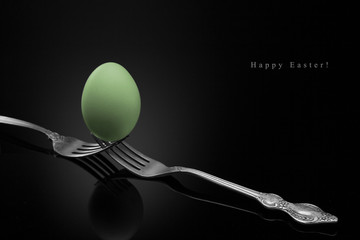 Happy Easter,green egg two forks ancient silver on a black background.