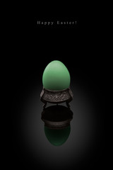 Happy Easter, green egg in an ancient silver coaster on a black background.