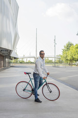 A young stylish man with sunglasses posing next to his bicycle.