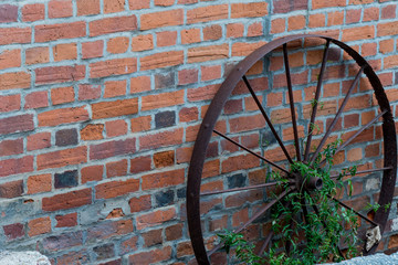a rusty metal wagon wheel against a brick wall