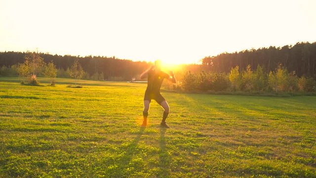 Young athlete doing exercises in beautiful meadow at sunset. Moving the camera. 4K