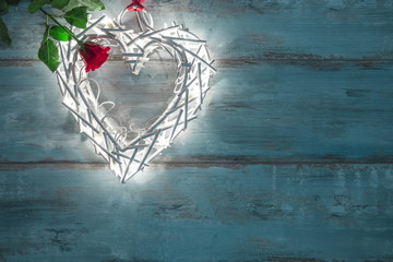 Valentines illuminations in the shape of a heart on a wooden background and red rose.