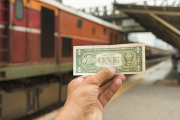 Hand holding dollar money with a train in background