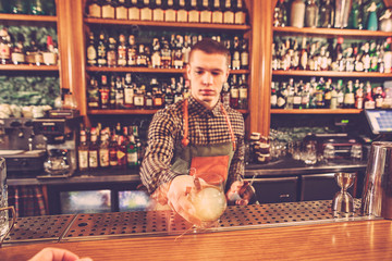 Barman making an alcoholic cocktail at the bar counter on the bar background