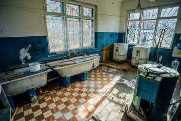 Old laundry room with a dirty floor and broken wash machines and bathes in an abandoned psychiatric hospital