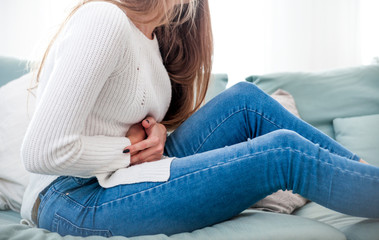 Woman suffering from abdominal pain while sitting on sofa at home