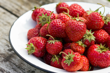 Fresh strawberries in white bowl on wooden background, rustic style.