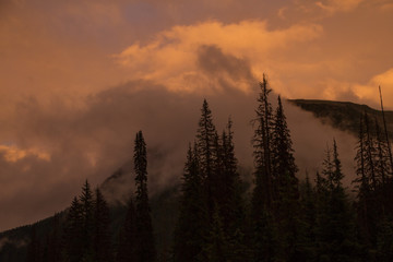Empty wet highway in Canada surrounded by mountains in clouds during orange sunset