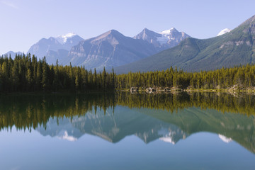 Reflection of Rocky Mountains in Herbert Lake in Canada on sunny day with clear sky