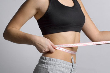 A girl in a sport suit will measure her waist with a flexible ruler.