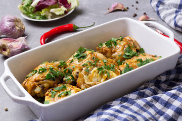 Chicken thighs gratin with sour cream and cheese, parsley, garlic, chilli pepper in the white baking dish.