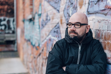 Obraz premium Bearded man standing leaning against a brick wall