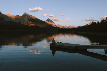 Man sitting on pier on Maligne lake in Rocky Mountains during colorful sunset with clouds