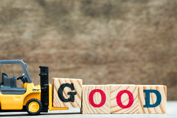 Yellow toy forklift hold letter block G to complete word good on wood background