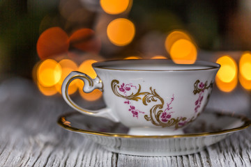 Empty Cup On Saucer on a wooden table with electric garland in bokeh with lights in defocused background