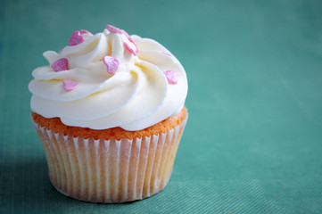 Cupcake for valentine's day with whipped cream and pink confectionery sprinkling In the form of hearts on blue background. Picture for a menu or a confectionery catalog.