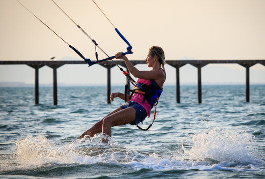 Kite surfing girl in sexy swimsuit with kite in sky on kiteboard in the blue sea riding waves saying hi. Recreational activity, water sports, action, hobby and fun in summer time. Kiteboarding sunset