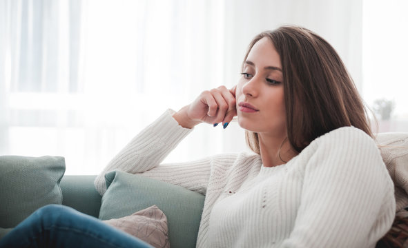 Sad woman sitting on sofa at home deep in thoughts, thinking concept