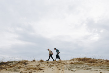 In search of adventures. Men are walking along the sandstone hill. Tourists are dressed in hipster jeans clothes, hats and trekking sneakers. A fascinating vacation in nature.