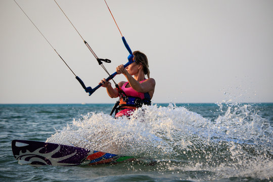Kite surfing girl in sexy swimsuit with kite in sky on kiteboard in the blue sea riding waves saying hi. Recreational activity, water sports, action, hobby and fun in summer time. Kiteboarding sunset