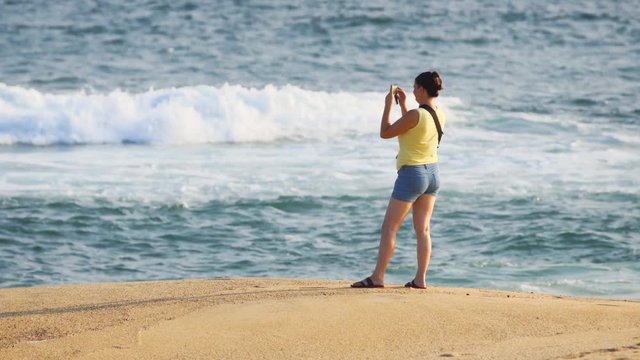Woman tourist makes a photo of the sea and beach using a smartphone
