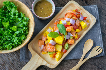 Top view of spicy salmon salad on wooden plate with lettuce