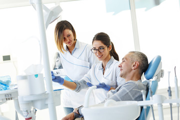 Obraz premium Dentist and her assistant in dental office talking with male patient and preparing for treatment.Examining x-ray image.