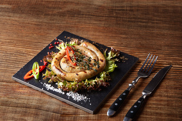 Baked homemade sausage close up on a black board, on wooden background.