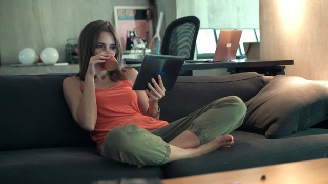 Happy woman watching movie on tablet sitting on sofa at home
