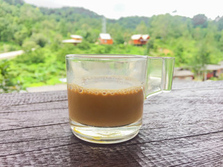 hot mocha coffee on wood table with village and forest background.
