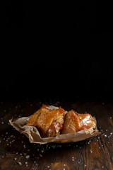 baked juicy chicken with a crispy crust, in spices, on a black plate, on baking paper, large sea salt on a dark wooden background