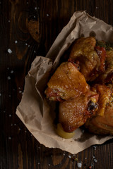 baked juicy chicken with a crispy crust, in spices, on a black plate, on baking paper, large sea salt on a dark wooden background