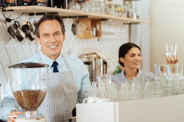 Can I help you. Pleasant handsome intelligent man looking straight smiling and standing in the kitchen.