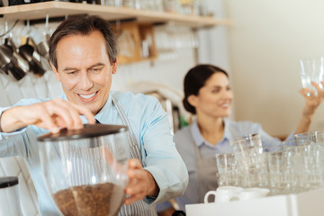 Fresh coffee. Interested responsible pleasant man standing in the kitchen smiling and making coffee.