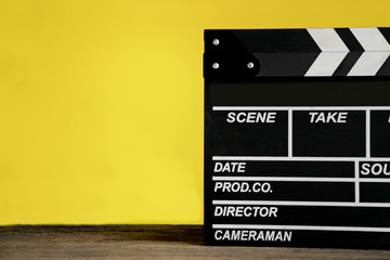 movie clapper on wood table with yellow background ; film, cinema and video photography concept